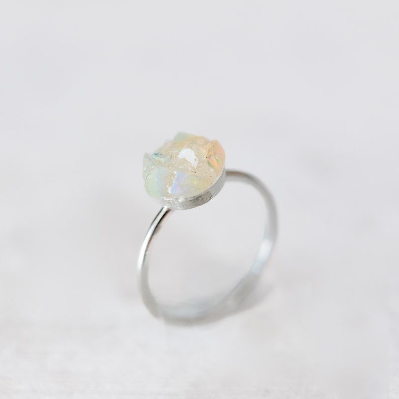 May include: A silver ring featuring a white opal gemstone set in the centre. The opal has an irregular shape and a milky white colour with iridescent flashes of colour.