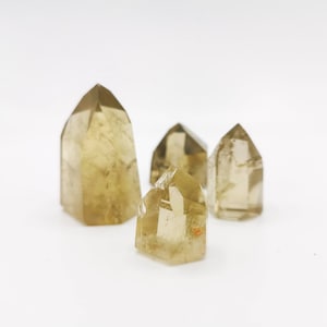 May include: Four clear quartz crystal points with a golden yellow hue. The crystals are arranged in a cluster on a white surface.