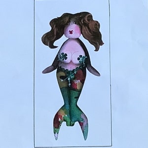 May include: A whimsical mermaid illustration with brown wavy hair, a pink face, and a red mouth. The mermaid's top is adorned with green floral accents, and her tail features a colourful patchwork design in shades of green, red, and yellow.