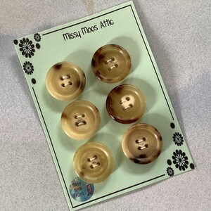 May include: Six brown and tan plastic buttons with two holes each. The buttons are arranged in two rows of three on a green card with the text "Missy Moos Attic" printed on the top.