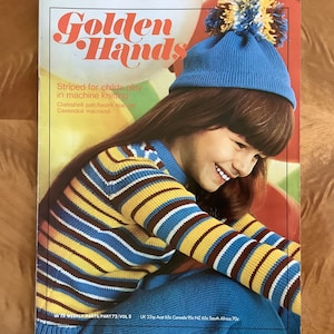 May include: A young girl wearing a blue and yellow striped sweater with a blue knit hat with a pom-pom on top. The magazine cover reads "Golden Hands" and "Striped for childs play in machine knitting".