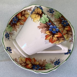 May include: A white teacup and saucer with a floral pattern of orange, yellow, green, and blue leaves and flowers. The cup and saucer have a scalloped edge.