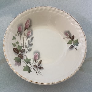May include: A white ceramic bowl with a gold rim and a floral design featuring pink roses and green leaves.