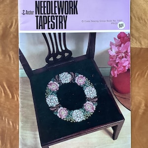 Pode incluir: Uma capa de livro vintage de tapeçaria de agulha que apresenta uma cadeira com uma coroa de flores bordada no assento. O livro é intitulado "Needlework Tapestry" e é do grupo Coats Sewing. O preço é de 60 centavos.