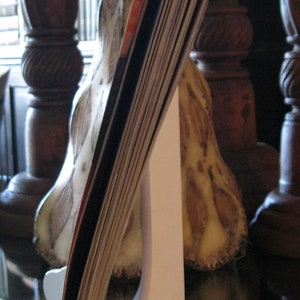 May include: A white card holder stand with a stack of cards leaning against it. The stand is made of wood and has a simple design. The cards are a variety of colors and sizes.