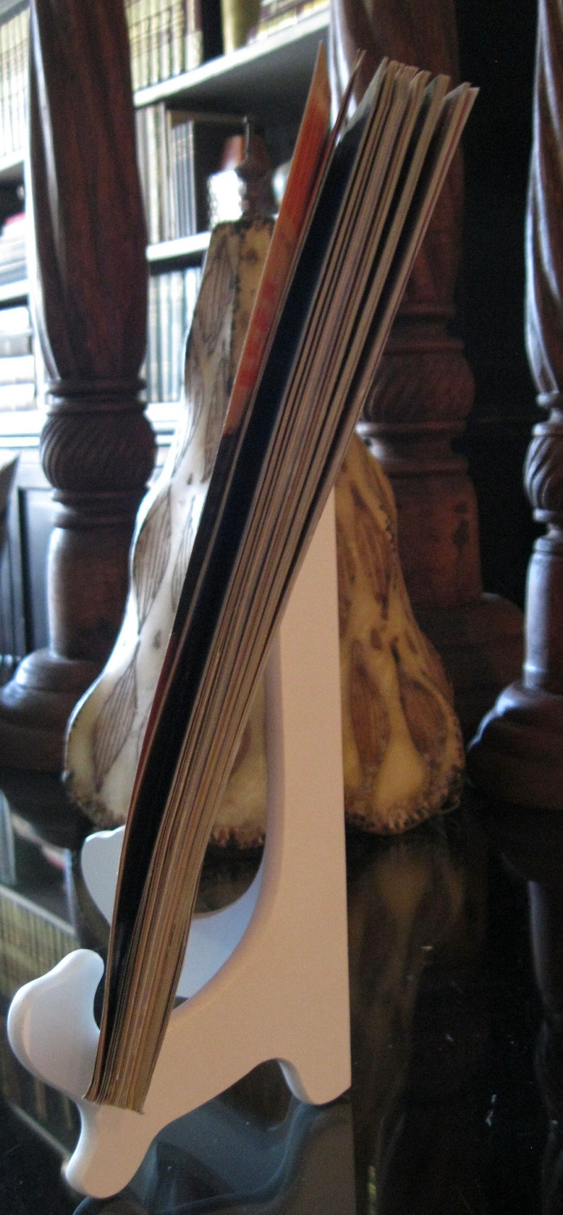 May include: A white card holder stand with a stack of cards leaning against it. The stand is made of wood and has a simple design. The cards are a variety of colors and sizes.