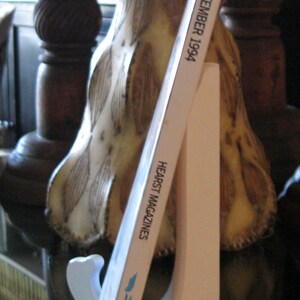 May include: A white magazine stand with a magazine titled "Cosmopolitan" September 1994, Hearst Magazines. The magazine is leaning against a decorative lamp with a white and brown patterned design.