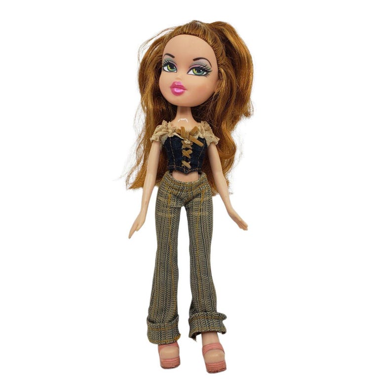 May include: A Bratz doll with auburn hair and green eyes. The doll wears a dark blue corset top with tan accents and brown plaid pants. The doll is wearing pink platform shoes.