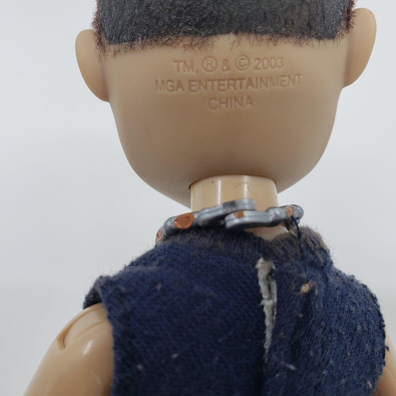 May include: Close-up of a doll's head and upper body. The doll has tan skin, black hair, and is wearing a dark blue top. The text "TM, &reg; & &copy; 2003 MGA ENTERTAINMENT CHINA" is printed on the back of the doll's head.