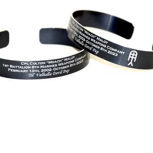 May include: Two black metal bracelets with engraved text. The text reads "CPL COLTON "MOACH" MALOY 1ST BATTALION 6TH MARINES WEAPONS COMPANY FEBRUARY 13TH, 2002-OCTOBER 8TH 2023 Til Valhalla Devil Pup".