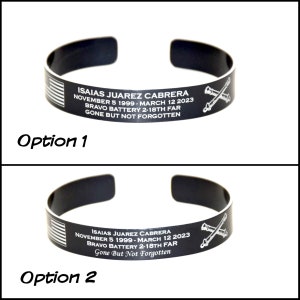 May include: Black metal cuff bracelet with engraved text and graphics. The text reads "ISAIAS JUAREZ CABRERA NOVEMBER 5 1999 - MARCH 12 2023 BRAVO BATTERY 2-18TH FAR GONE BUT NOT FORGOTTEN." Includes an American flag and crossed cannons.