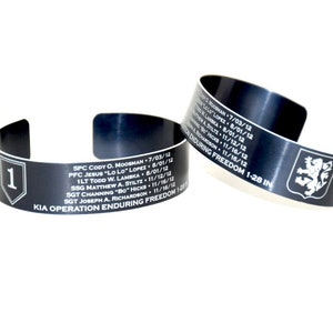 May include: Two black metal bracelets with engraved names and dates. The bracelets commemorate soldiers who died in Operation Enduring Freedom. One bracelet has the number "1" and the other has a lion emblem.