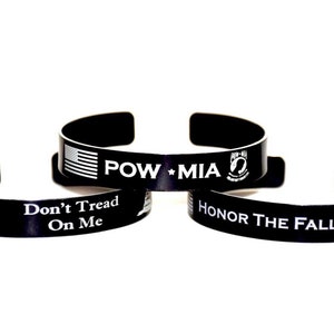 May include: Three black metal bracelets with white text and images. The bracelets read "Don't Tread On Me", "POW * MIA", and "Honor The Fallen".