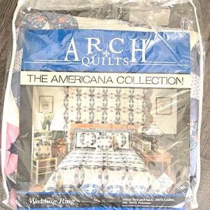 以下が含まれることがあります： 「The Americana Collection」のArch Quiltsブランドのベッドリネンセット。パッケージには「Wedding Ring」柄のキルトと枕が写った寝室の様子が印刷されています。ラベルには、表面と裏面が綿100%、中綿がポリエステル100%であると記載されています。