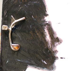 Puede incluir: Una pintura abstracta en blanco y negro de una cara con un gancho de metal plateado sujeto al lado.