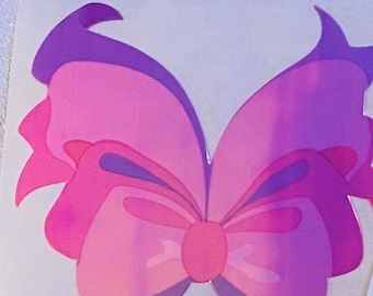 May include: A pink and purple butterfly-shaped bow with a large, round center. The bow is made of a shiny, iridescent material.
