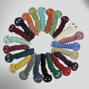 Puede incluir: Una colección de 24 juguetes de gusano de crochet con ojos saltones en varios colores, incluyendo rojo, verde, azul, amarillo y morado.