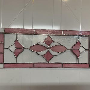 May include: A rectangular stained glass panel with a floral design. The panel features a border of pink and white glass, with a central design of pink and white flower-like shapes. The glass is set in a metal frame.