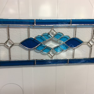 May include: A stained glass window panel with a geometric design featuring blue and clear glass pieces. The panel is framed in silver metal.