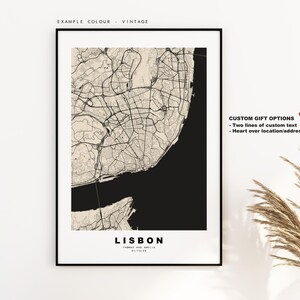 May include: A black and white map of Lisbon, Portugal with the city name and the text "Thomas and Amelia" printed below. The map is framed in a black frame and is hanging on a white wall. The text "Custom Gift Options" is printed on the right side of the image with the text "Two lines of custom text" and "Heart over location/address" printed below.
