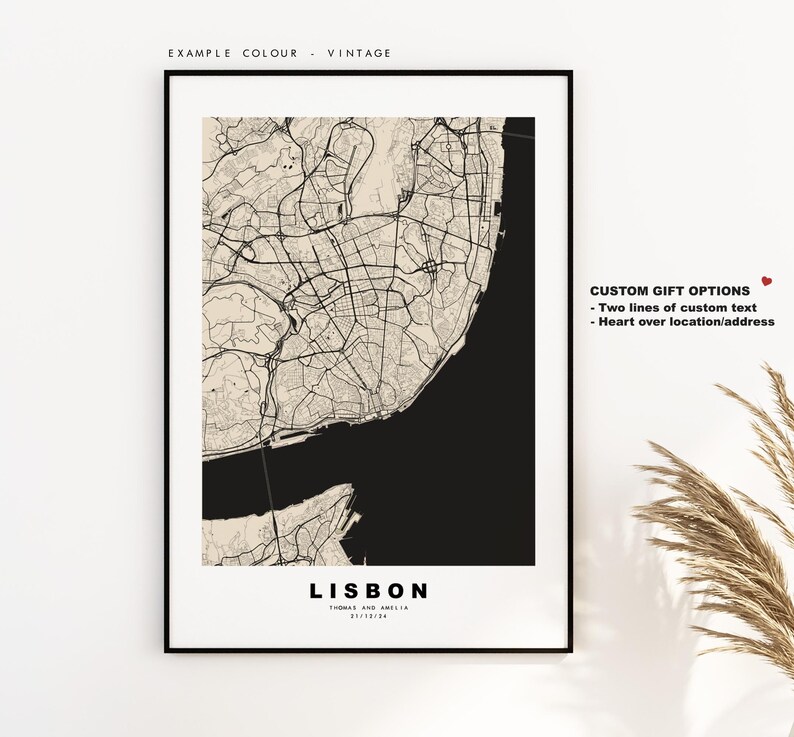 May include: A black and white map of Lisbon, Portugal with the city name and the text "Thomas and Amelia" printed below. The map is framed in a black frame and is hanging on a white wall. The text "Custom Gift Options" is printed on the right side of the image with the text "Two lines of custom text" and "Heart over location/address" printed below.
