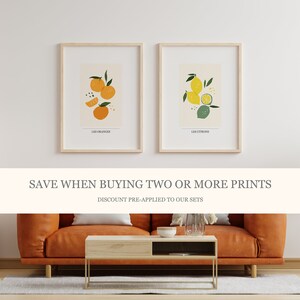 May include: Two framed prints with illustrations of oranges and lemons. The prints are on a white background with the text "Les Oranges" and "Les Citrons" below the illustrations. The text "SAVE WHEN BUYING TWO OR MORE PRINTS" is displayed in a white banner below the prints. The text "DISCOUNT PRE-APPLIED TO OUR SETS" is displayed below the banner.
