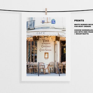 May include: A Parisian cafe with a white awning and a sign that reads "Cafe". The sign also says "Vins de Propriete Cocktails Cuisine Soignee". There are tables and chairs outside the cafe.