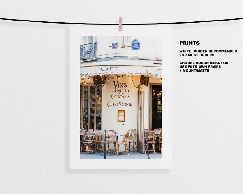 May include: A Parisian cafe with a white awning and a sign that reads "Cafe". The sign also says "Vins de Propriete Cocktails Cuisine Soignee". There are tables and chairs outside the cafe.