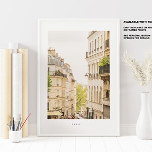 May include: A framed print of a Parisian street scene with buildings in a warm yellow color. The text "PARIS" is at the bottom of the print. The text "AVAILABLE WITH TEXT ONLY AVAILABLE ON PRINTS OR FRAMED PRINTS SEE PERSONALISATION OPTIONS FOR DETAILS" is in the top right corner of the print.