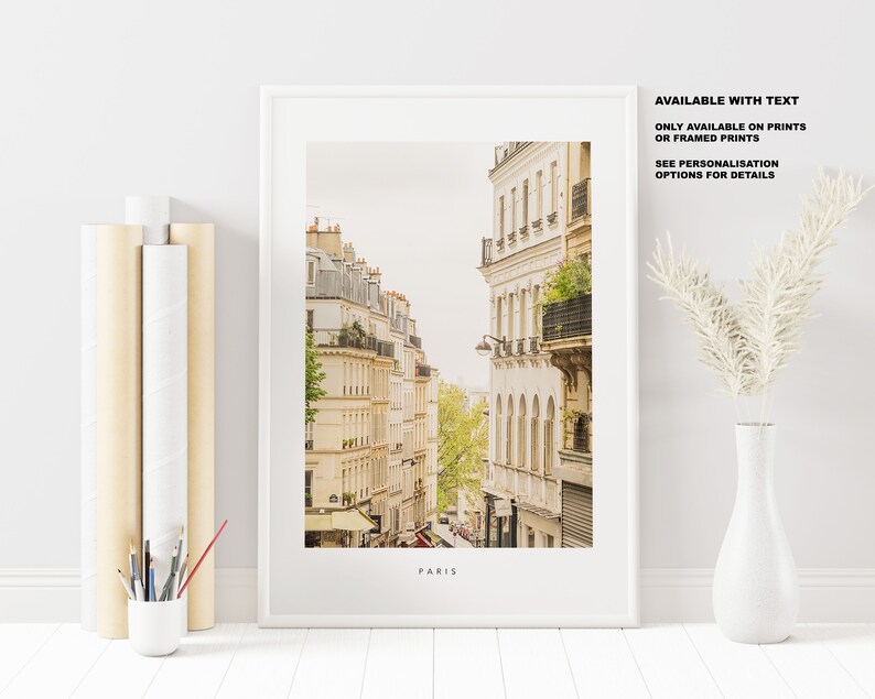 May include: A framed print of a Parisian street scene with buildings in a warm yellow color. The text "PARIS" is at the bottom of the print. The text "AVAILABLE WITH TEXT ONLY AVAILABLE ON PRINTS OR FRAMED PRINTS SEE PERSONALISATION OPTIONS FOR DETAILS" is in the top right corner of the print.