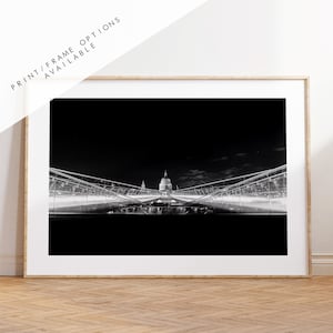 Puede incluir: Una fotografía en blanco y negro de un puente sobre un río con un edificio en el fondo. El puente está iluminado con luces, y el edificio también está iluminado. La foto fue tomada de noche.