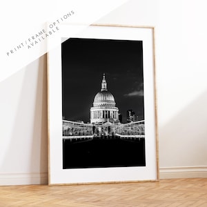 May include: A black and white photograph of St. Paul's Cathedral in London, England at night. The cathedral is illuminated, and the surrounding area is dark.
