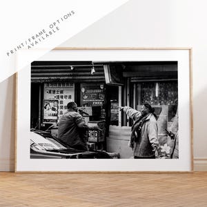 May include: Black and white photograph of two people in an urban setting. One person is pointing, while the other is seated. The image is framed and includes text: "PRINT/FRAME OPTIONS AVAILABLE."