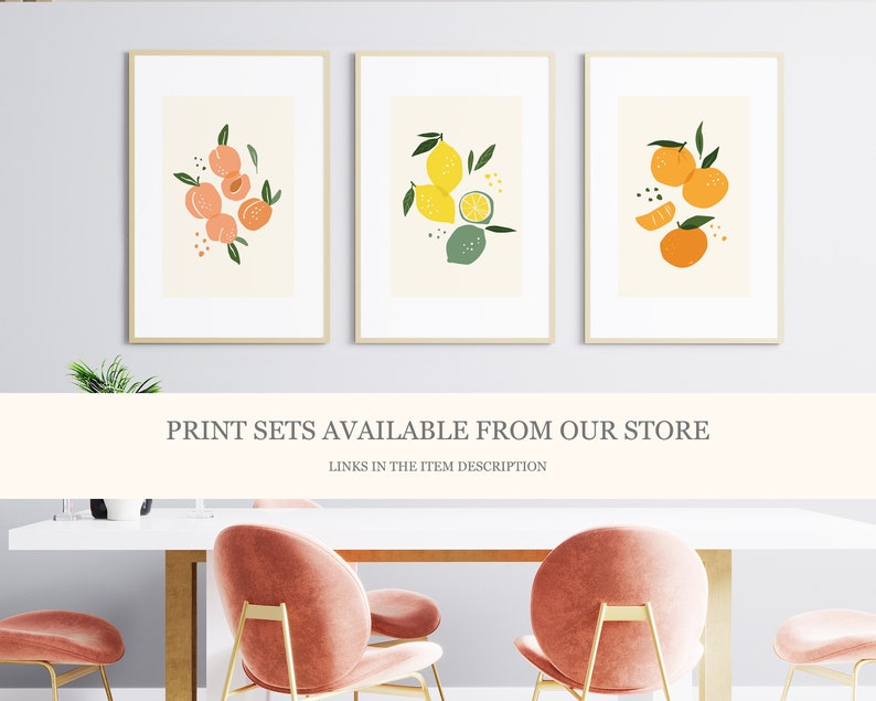 May include: Three framed prints with illustrations of fruit. The first print features peaches, the second print features lemons and limes, and the third print features oranges. The prints are displayed on a white wall above a white table with pink chairs.