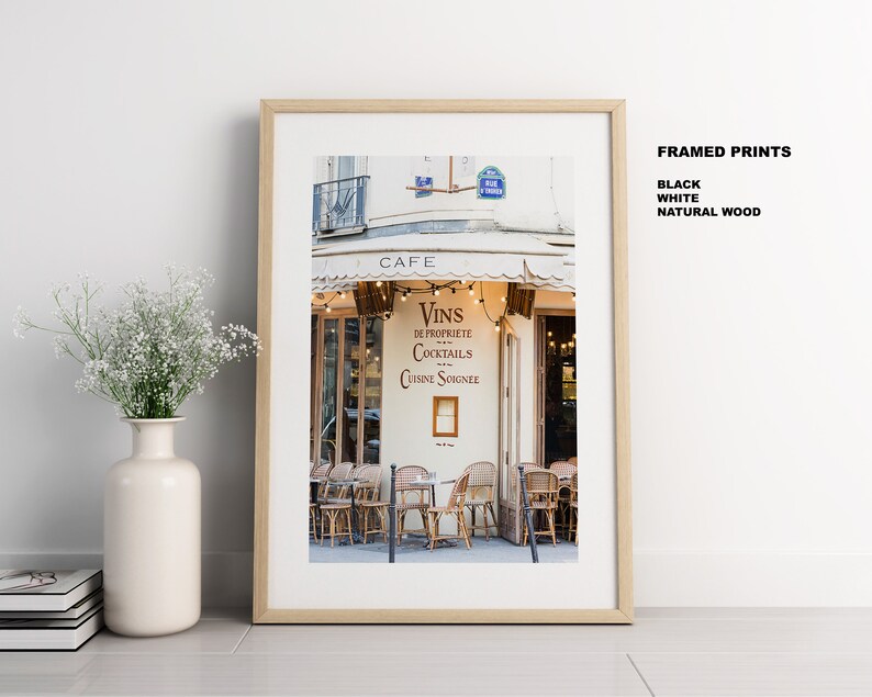 May include: A framed photograph of a Parisian cafe with a white awning and string lights. The cafe sign reads "Cafe" and "Vins de Propriete Cocktails Cuisine Soignee".