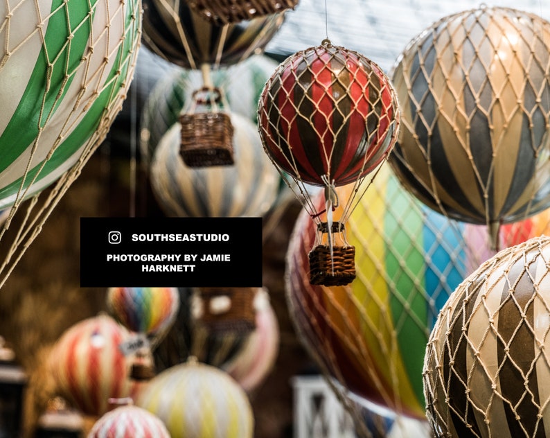 May include: A collection of colorful hot air balloons with various patterns and designs, including stripes, polka dots, and a checkered pattern. Some balloons have a basket attached to the bottom.