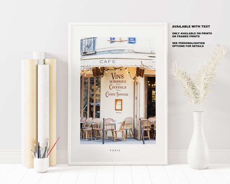 May include: A framed print of a Parisian cafe with a white awning and a sign that reads "Cafe, Vins de Propriete, Cocktails, Cuisine Soignee". The cafe has a few tables and chairs outside, and the street is cobblestone. The print is titled "Paris".