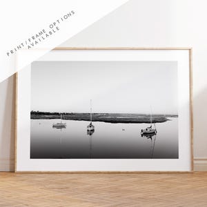 May include: A black and white photograph of three sailboats anchored in a calm body of water. The sailboats are silhouetted against a cloudy sky.