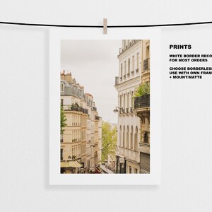 May include: A photograph of a narrow street in Paris, France. The street is lined with tall, beige buildings with balconies and windows. The buildings are decorated with ornate details, such as wrought iron railings and decorative stonework. The street is empty, except for a few trees and a small amount of foliage.