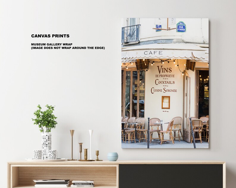 May include: A Parisian cafe with a white awning and a sign that reads "Cafe" and "Vins de Propriete Cocktails Cuisine Soignee". The cafe has a string of lights hanging above the entrance and tables and chairs are set up outside.