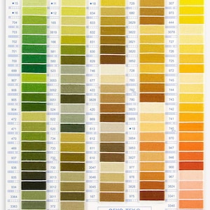 Op de afbeelding: Een DMC-kleurenkaart met rijen garenstalen in verschillende tinten groen, geel, oranje en bruin. De kaart is gelabeld met nummers en het DMC-logo. De tekst "OEKO-TEX&reg; CONFIDENCE IN TEXTILES STANDARD 100% CQ 514/2 IFTH" is op de kaart gedrukt.