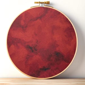 Peut inclure: Un tambour à broder circulaire en bois contenant un tissu au motif nuageux marbré rouge foncé et noir. Le tissu est tendu dans le cadre, qui présente une vis de serrage de couleur or métallique sur la partie supérieure de l'objet.