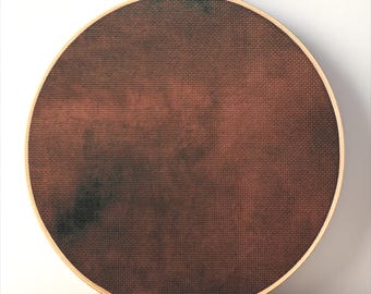 May include: A circular wooden embroidery hoop containing a piece of fabric with a mottled, dark brown and black tie-dye pattern. The hoop features a gold-toned metal tightening screw at the top, securing the fabric firmly within the frame.