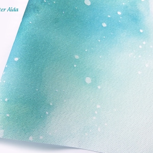 May include: A sheet of Aida fabric featuring a gradient watercolor design that transitions from deep teal to light aqua. The surface is speckled with white glitter accents and includes the text Glitter Aida in the upper left corner.