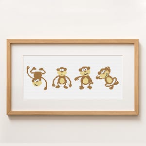 May include: A framed cross-stitch artwork featuring four cartoon monkeys in various poses. The monkeys are brown and tan, with white accents, and are set against a white background. The frame is made of light-colored wood.