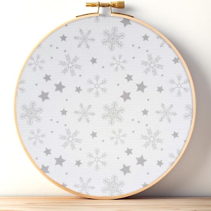 May include: A round embroidery hoop with a white fabric featuring a pattern of gray snowflakes and stars. The wooden hoop is secured with a brass screw. The design is perfect for winter-themed crafts.