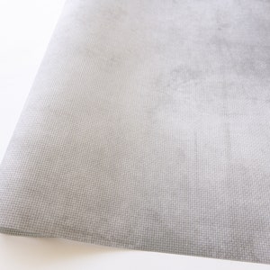 Op de afbeelding: Een close-up van een grijze, textuurrijke stof met een subtiel geweven patroon. De stof is dubbelgevouwen en lijkt zacht en glad.