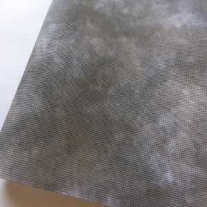 May include: A piece of gray fabric with a mottled, cloud-like pattern and a visible woven grid texture. The material features subtle variations in tone, ranging from dark charcoal to lighter, muted gray shades across the surface.