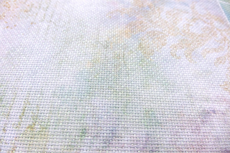 May include: Close-up of a white fabric with a fine weave. The fabric has a subtle, faded pattern of light green, yellow, and brown.