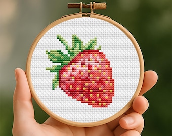May include: A cross-stitch embroidery hoop featuring a detailed strawberry design. The strawberry is rendered in shades of red, pink, and yellow, with green leaves. The embroidery is set against a white background, held in a wooden hoop.